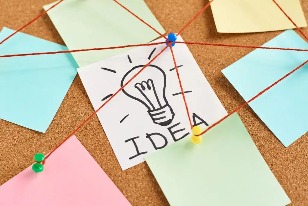 Painted light bulb with the word idea and colored blank notes on a cork board