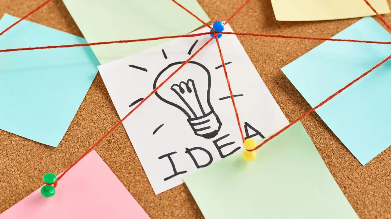 Painted light bulb with the word idea and colored blank notes on a cork board